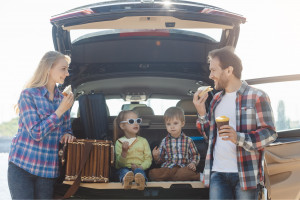 Family eating healthy food at the rear of their car during a road trip